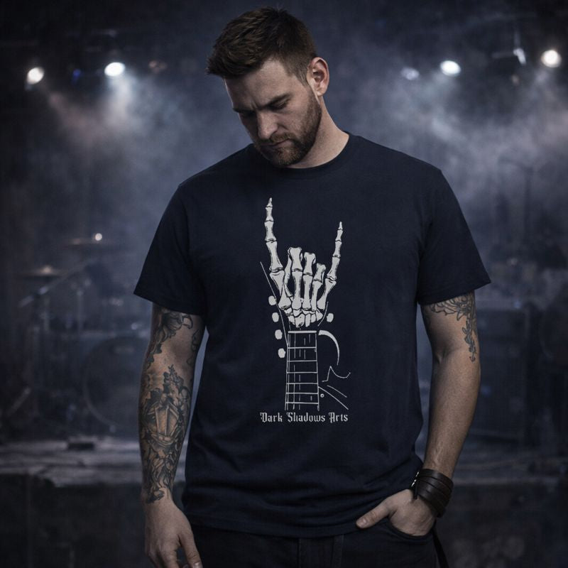 Gothic Rock T-Shirt „Bones of Rock“ von Dark Shadows Arts mit Skelett-Gitarrenhand im Devil-Horns-Zeichen, getragen von Model auf dunkler Konzertbühne