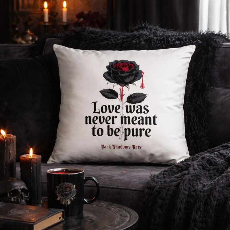 Weißes Dekokissen mit Dark Romantic Motiv „Love Was Never Meant to Be Pure“, schwarze Rose mit rotem Tropfen und Gothic Statement, inszeniert auf dunklem Sofa mit Kerzen im stimmungsvollen Gothic Interior, Design von Dark Shadows Arts