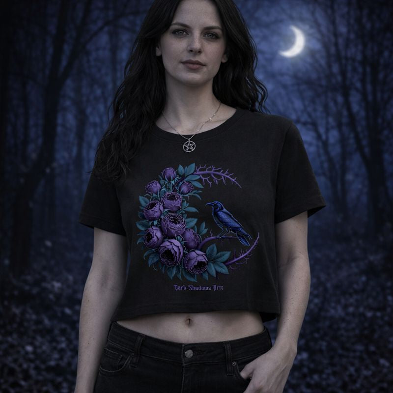 Schwarzes Ladies Cropped Tee mit Gothic Motiv „Moonlit Mourning“, violette Rosen im floralen Dornenkreis mit Rabe, getragen von weiblichem Model im nächtlichen Wald bei Mondlicht, Dark Romantic Design von Dark Shadows Arts