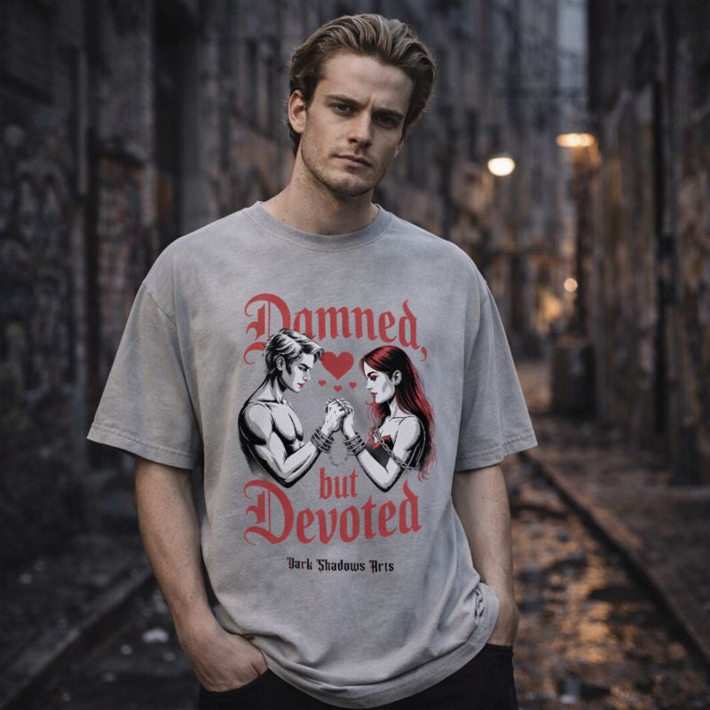 Oversized Shirt von Dark Shadows Arts mit Motiv „Damned but Devoted“ – Gothic Mann trägt graues Oversized T-Shirt mit Dark Romance Liebespaar und Kettenmotiv, urbanes düsteres Street-Setting