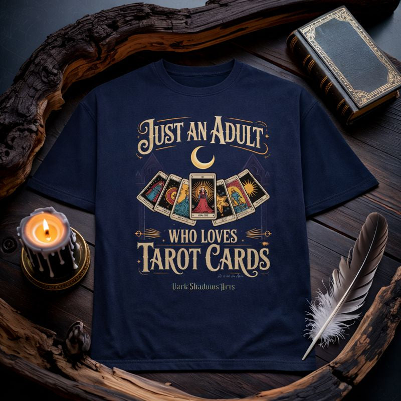 Dark Shadows Arts Premium T-Shirt „Just an Adult Who Loves Tarot Cards“ mit Tarotkarten-Motiv auf dunklem Stoff, mystisches Gothic Flatlay Mockup mit Kerze, Feder und Buch