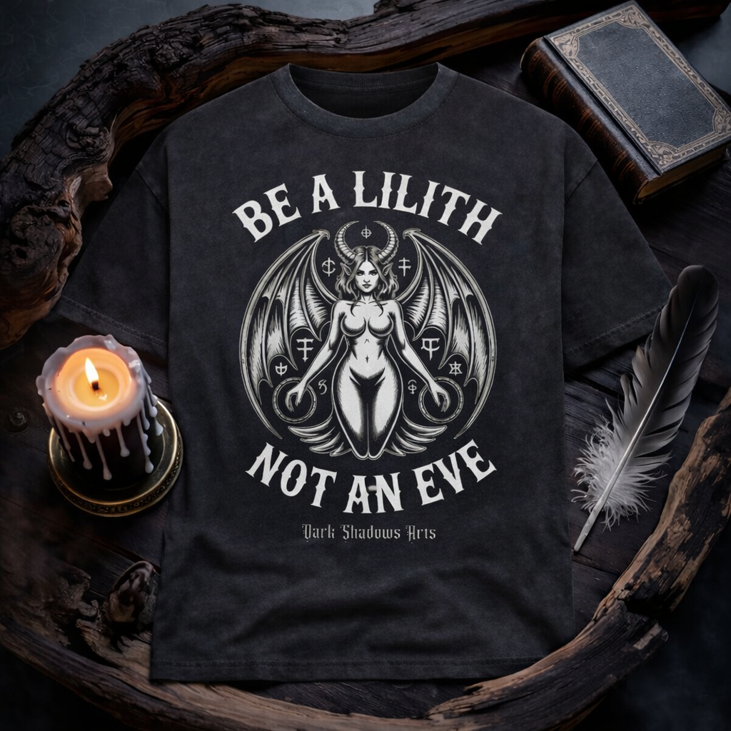 Dark Shadows Arts Heavy Oversized Shirt „Lilith – Die Urfigur der Nacht“ mit kraftvoller Lilith Illustration, Fledermausflügeln und okkulten Symbolen im Gothic Stil, präsentiert im dunklen Holz-Mockup mit Kerze, Feder und altem Buch.