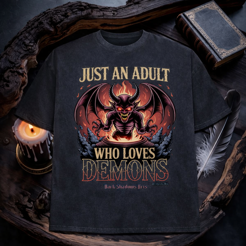 Just an Adult Who Loves Demons Heavy Cotton Oversized Shirt von Dark Shadows Arts im düsteren Flatlay Mockup mit Kerzenlicht, altem Buch und mystischer Atmosphäre – Demon Motiv mit Flammen und Hörnern auf charcoal grauem Oversized Shirt